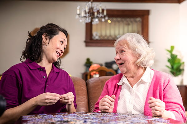 Aging woman and Care Professional work on puzzle together at home