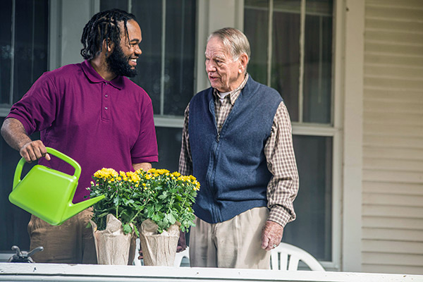 Care Professional and aging man water flowers outside