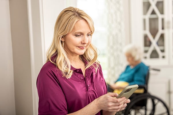 Care Professional reviews mobile app with senior woman sitting in background