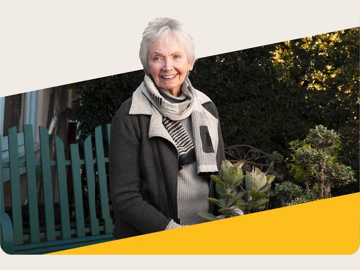 Senior woman smiles and holds potted plant in garden